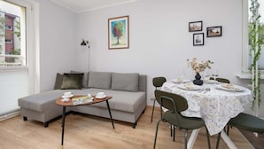 A modern living room with a grey sofa, a small round table with a magazine, and a dining area with a round table set for two.