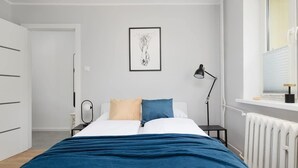 A bedroom with a bed, bedside tables, a radiator, a window, and a framed artwork on the wall.