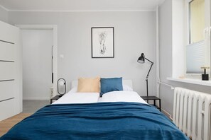 Ein Schlafzimmer mit einem Bett, Nachttischen, einem Heizkörper, einem Fenster und einem gerahmten Kunstwerk an der Wand.