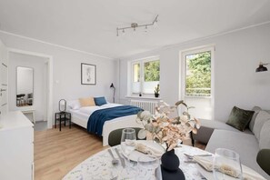 A modern bedroom with a bed, bedside table, and a dining area with a table set for two.