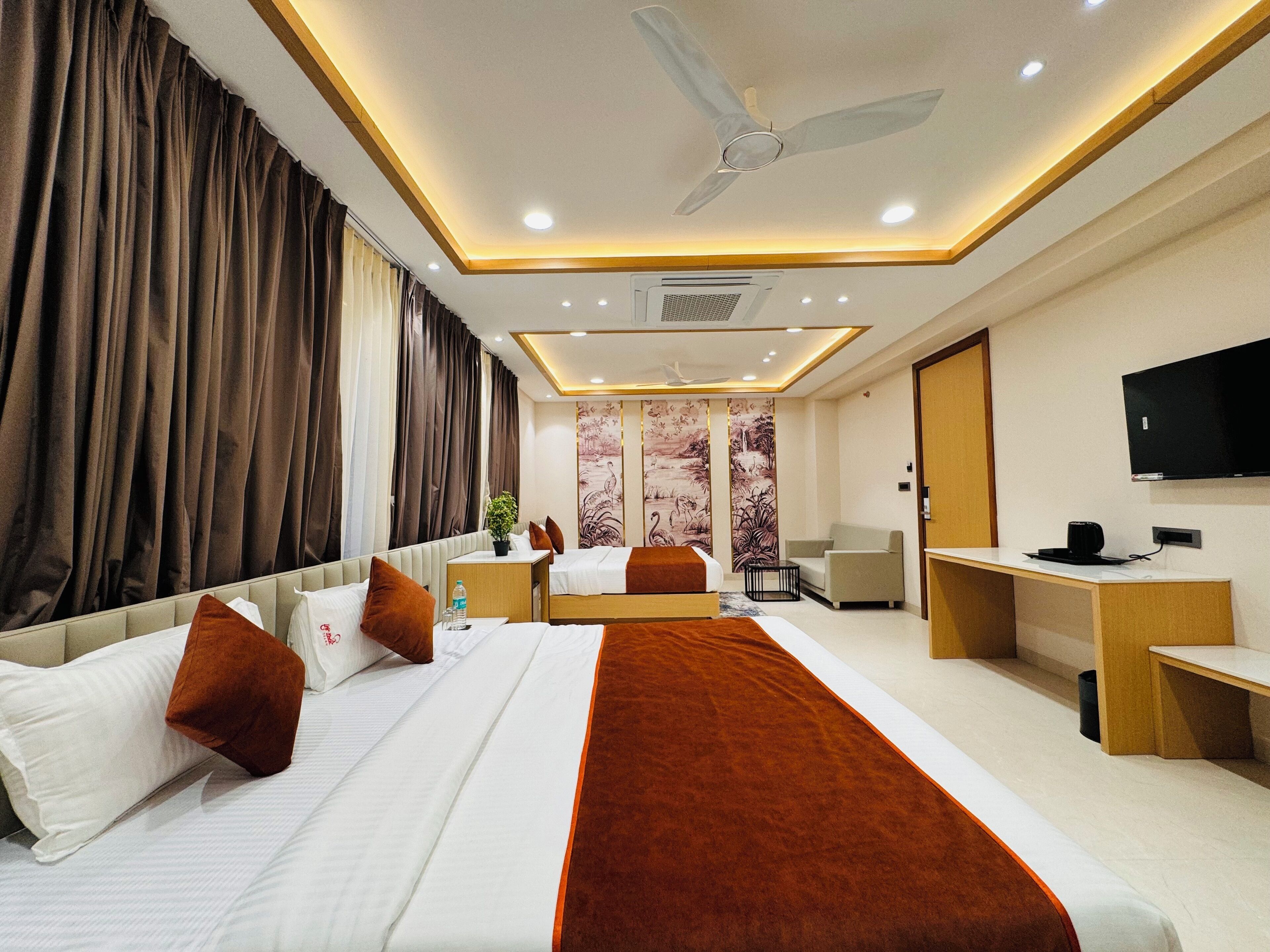 A hotel room with a large bed, a desk, a chair, a TV, and a ceiling fan.