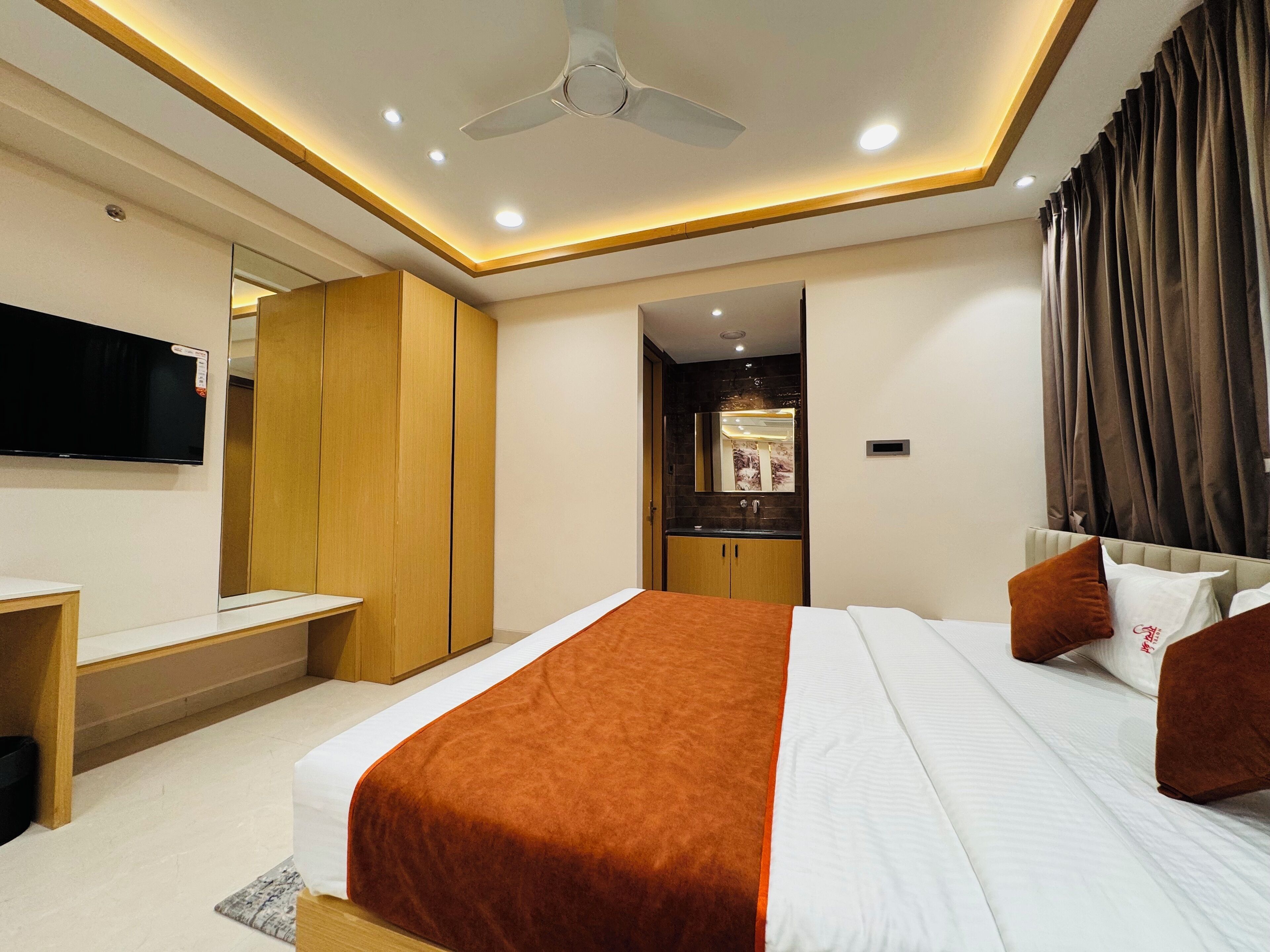 Camera d'hotel moderna con un letto grande, televisione a schermo piatto, armadio in legno e bagno con specchio e lavandino.