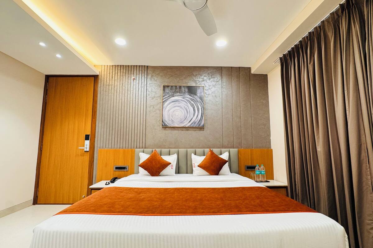 A hotel room with a large bed, a ceiling fan, a wall-mounted painting, and a wooden door.