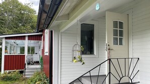 Une maison à l’extérieur blanc, avec une porte rouge, un petit porche avec des marches et une cage à oiseaux décorée de fleurs.