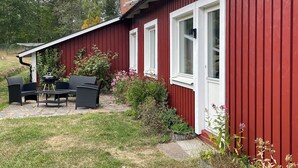 Un bâtiment rouge avec des ornements blancs, une terrasse dotée de mobilier d’extérieur et un jardin où poussent diverses plantes et fleurs.