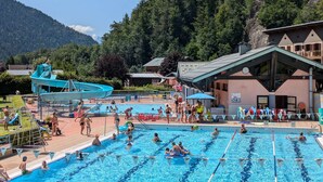 Une piscine dotée de plusieurs couloirs, entourée d’une zone de détente avec des chaises longues et un toboggan aquatique.