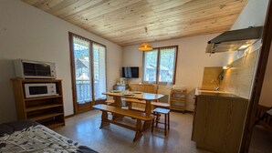 Une pièce confortable avec un plafond en bois, une table à manger avec des bancs, un four à micro-ondes, une télévision et un coin cuisine.