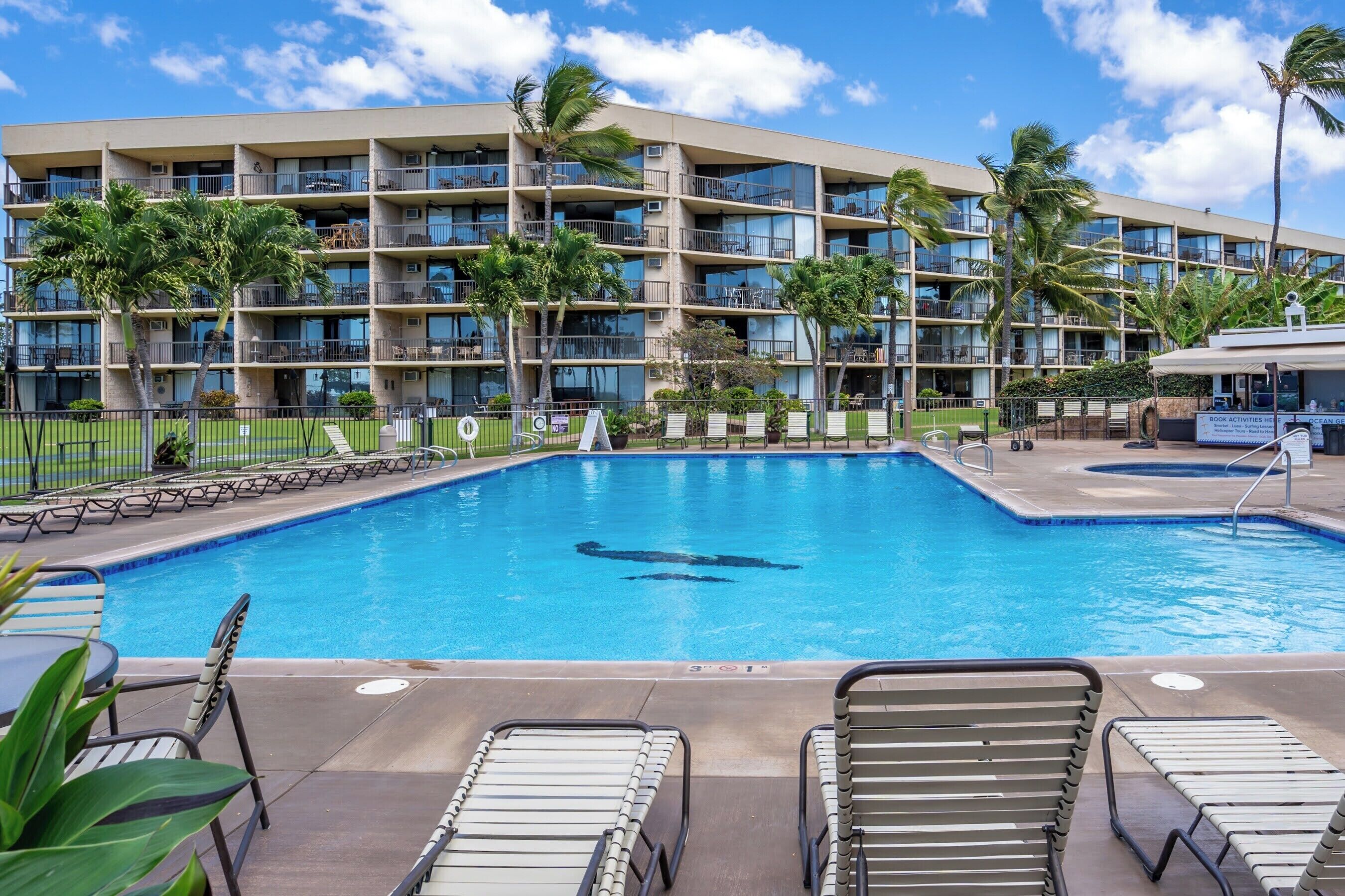 A hotel with a swimming pool, multiple balconies, and palm trees.
