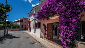 Una strada con un edificio ricoperto di fiori viola, un segnale di stop e un cielo azzurro intenso.
