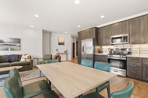 A modern kitchen with wooden cabinets, stainless steel appliances, and a dining area with a wooden table and chairs. - Central Location, Private Balcony and Mountain Views, Cozy Gas Fireplace (Silverthorne)