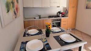 A dining area with a table set for four, equipped with plates, cutlery, and glasses. There are two chairs, a coffee machine, and a stove in the background.