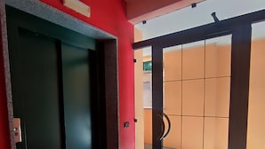 A hallway with a red wall, a black elevator, and a glass door leading to an orange room.