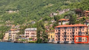 A coastal town with buildings along the waterfront, featuring balconies and a hillside backdrop.