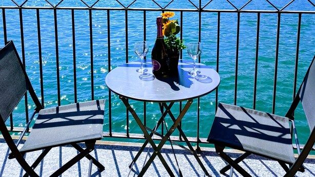 A terrace with two chairs and a table, overlooking a lake with mountains in the background.