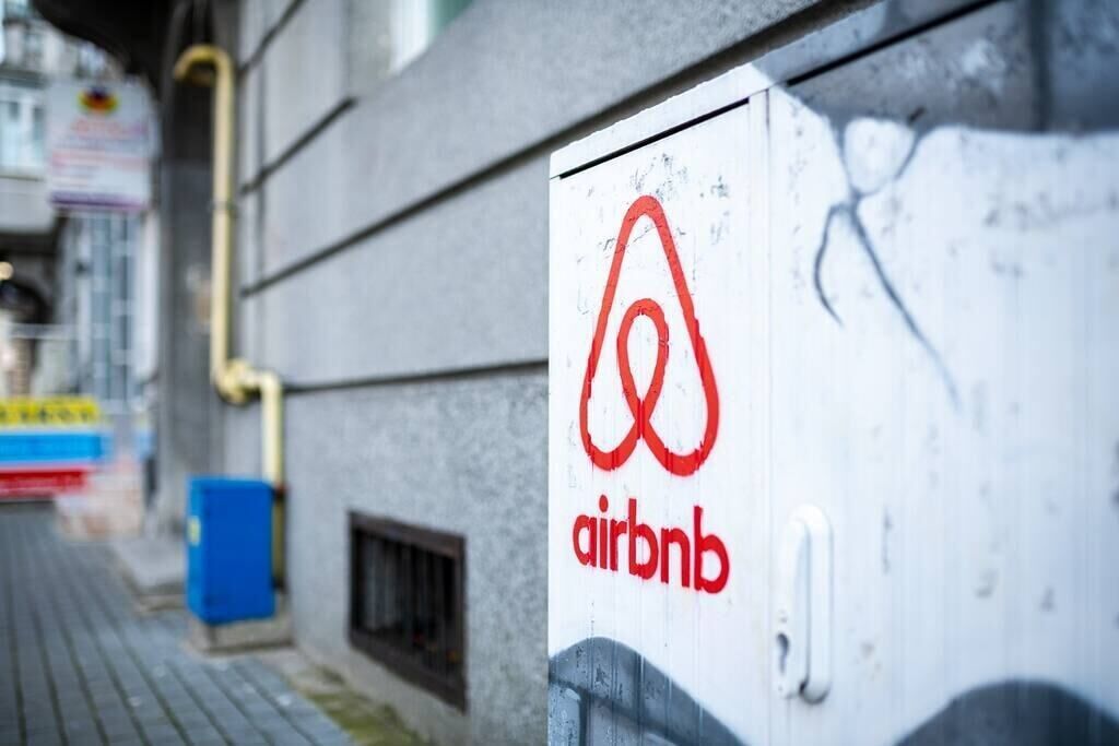 Un panneau blanc avec le logo rouge d’Airbnb, fixé sur un mur gris.