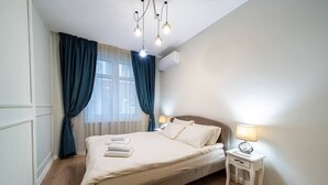 En snyggt bäddad säng med ett vitt täcke och kuddar, ett sängbord med en lampa och ett fönster med blå gardiner.