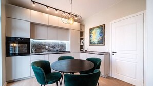 Ett modernt kök med inbyggda vitvaror, ett runt matbord med stolar och en stor tavla på väggen.