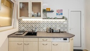 A kitchen with a sink, a scale, a kettle, and a toaster. There are cabinets with handles and a backsplash with a geometric pattern. - Roman Thermae Central Studio (Varna)