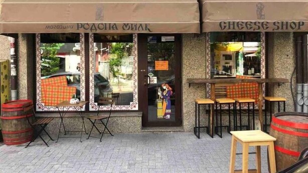 A storefront with a sign reading "Cheese Shop" and a window display featuring a person in traditional attire. - Roman Thermae Central Studio (Varna)
