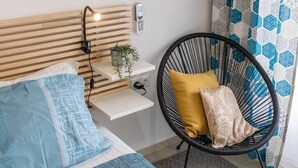 A bedroom with a bed, bedside table, lamp, phone, chair, and patterned curtains. - Roman Thermae Central Studio (Varna)