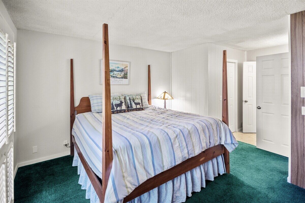 A bedroom with a four-poster bed, a green carpet, and a framed picture on the wall.