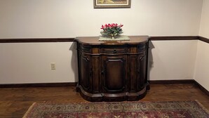 A corner room with a wooden cabinet, a framed painting, and a floral arrangement on the cabinet. - Lakefront Home in Cabot (Cabot)