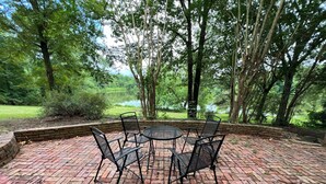 A brick patio with a round table and four chairs, surrounded by trees and a view of a lake. - Lakefront Home in Cabot (Cabot)