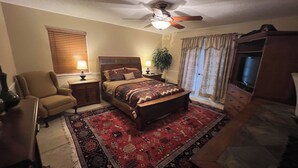 A bedroom with a bed, a chair, a TV, a ceiling fan, and a window with curtains. - Lakefront Home in Cabot (Cabot)