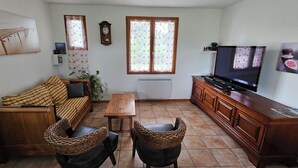 A living room with a sofa, two wicker chairs, a wooden coffee table, a TV, and a cabinet. - Gîte "Le Figuier (Villebernier)