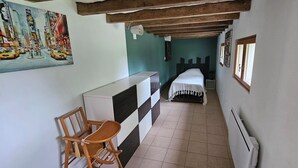 A narrow hallway with a bed, a small table, and a chair. - Gîte "Le Figuier (Villebernier)