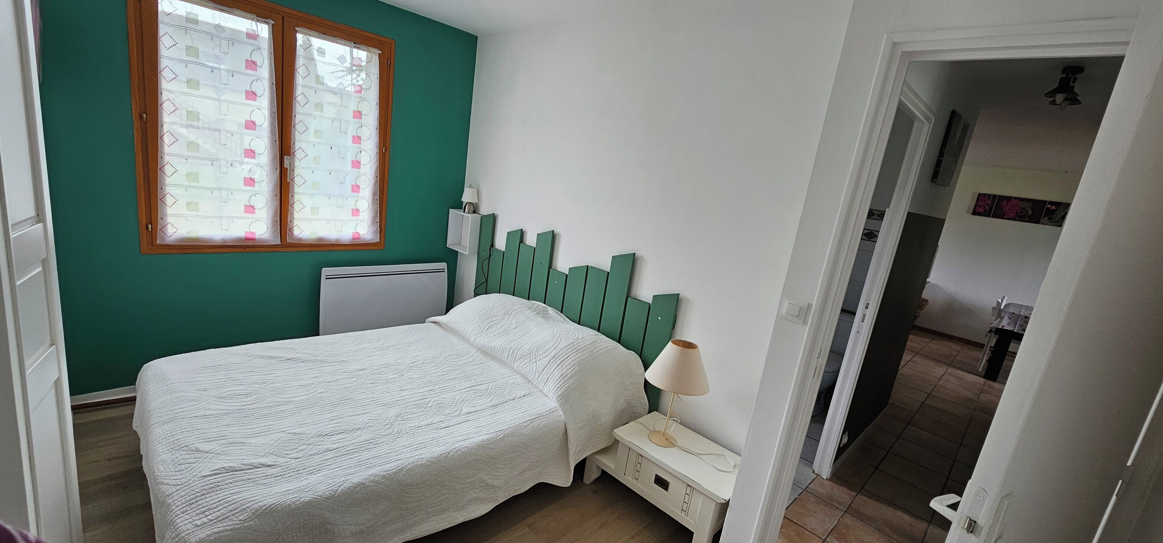 A bedroom with a bed, a nightstand, a window with blinds, and a green headboard.