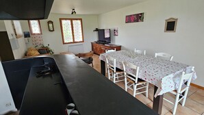 A kitchen with a long counter, a dining table with chairs, a television, and a window with curtains. - Gîte "Le Figuier (Villebernier)