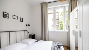 A bedroom with a bed, a bedside table, a lamp, and a window with curtains. - Native Apartments Żuławskiego 8A Deluxe (Kraków)