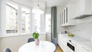 A modern kitchen with white cabinets, a marble countertop, and a round dining table with chairs. - Native Apartments Żuławskiego 8A Deluxe (Kraków)