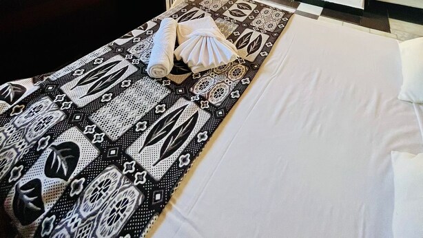 A single bed with a patterned bedspread, a TV mounted on the wall, and a small kitchenette area. - Pousada Novo Encanto Maresias (São Sebastião)