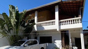 A two-story house with a white exterior, a balcony with white balustrades, and a white pickup truck parked in front. - Pousada Novo Encanto Maresias (São Sebastião)
