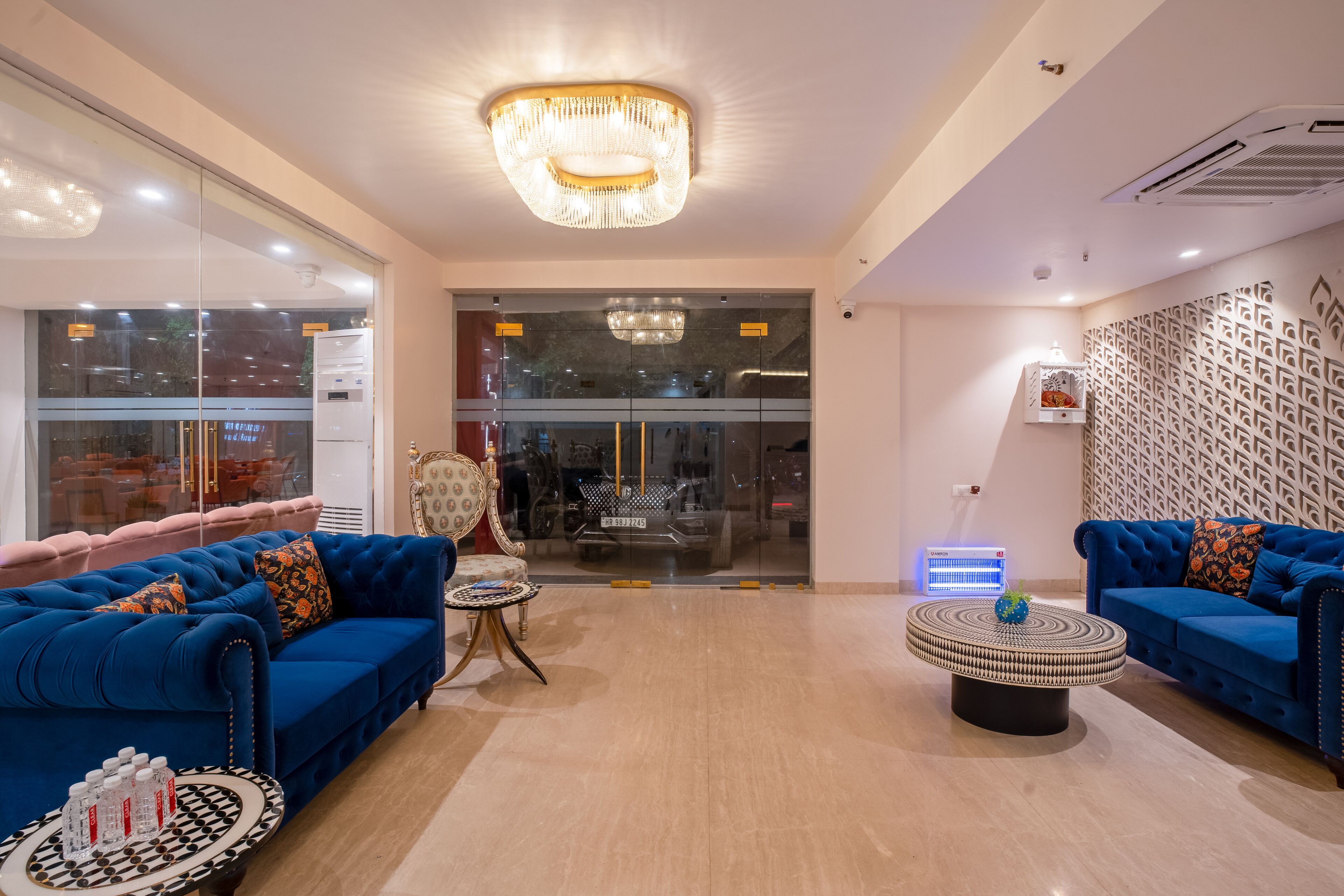 A modern hotel lobby with blue sofas, a round coffee table, and a chandelier.