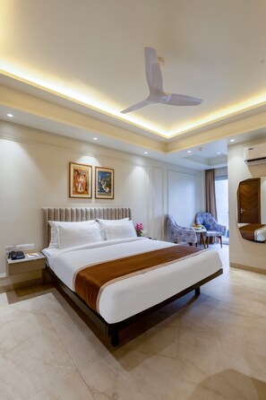 A modern hotel room with a large bed, a ceiling fan, a small table with chairs, and artwork on the walls. - Aadat Hotel Near Artemis Hospital Gurgaon (Gurugram)