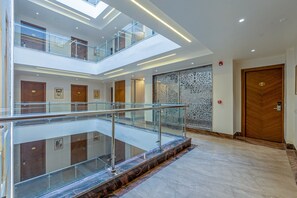 A multi-level interior with glass railings, wooden doors, and a patterned wall. - Aadat Hotel Near Artemis Hospital Gurgaon (Gurugram)