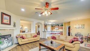 A spacious living room with a fireplace, a ceiling fan, and a dining area with a chandelier. - San Antonio Home - Outdoor Oasis & Greenbelt Views (San Antonio)