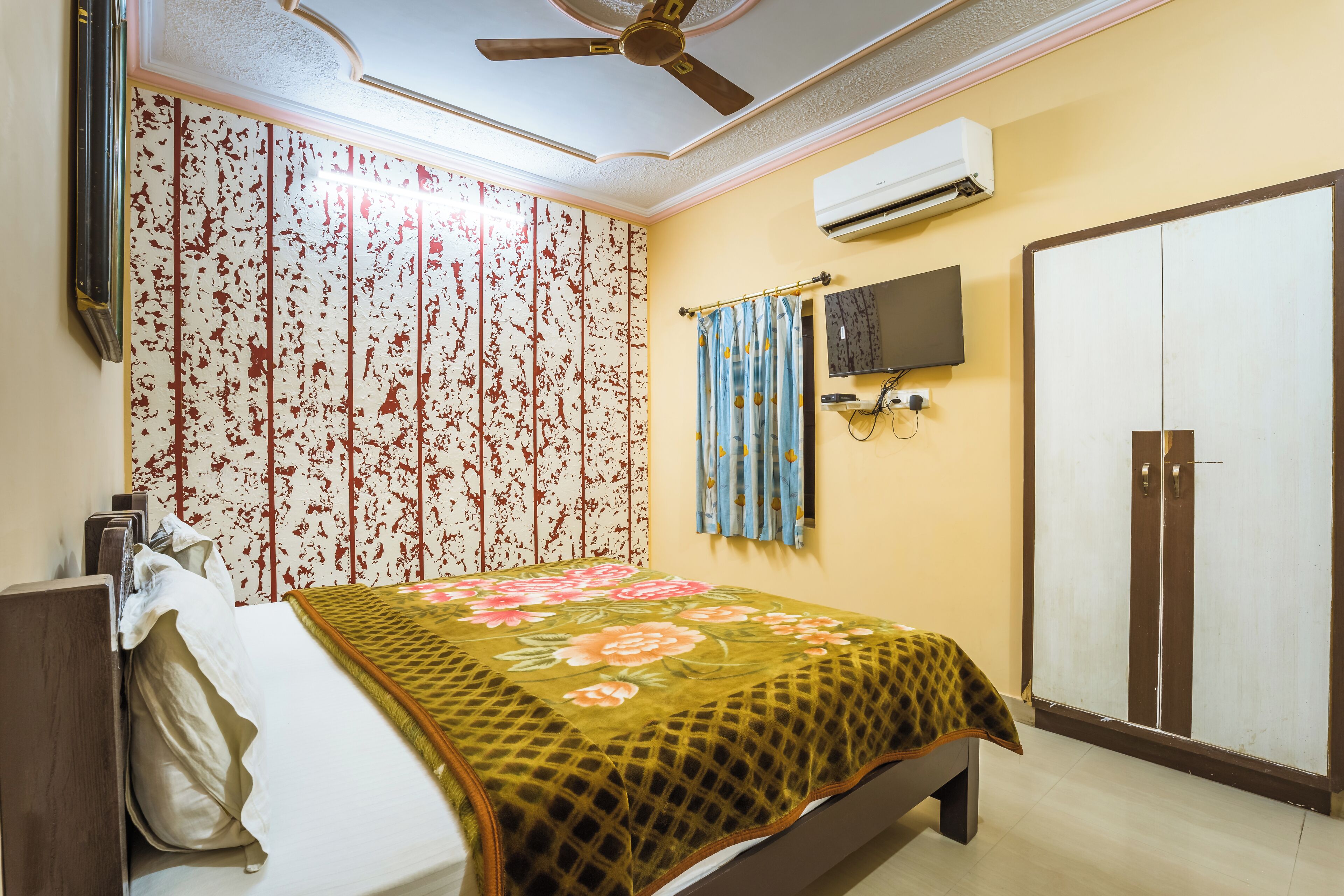 A bedroom with a bed, a wardrobe, an air conditioner, and a ceiling fan.