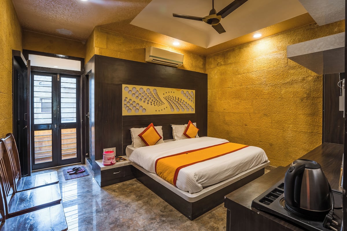 A hotel room with a bed, a desk, a chair, a ceiling fan, and a wall-mounted air conditioner.