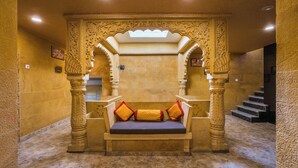 Een traditionele zithoek in Indiase stijl, met versierde pilaren en een bank met kussens.