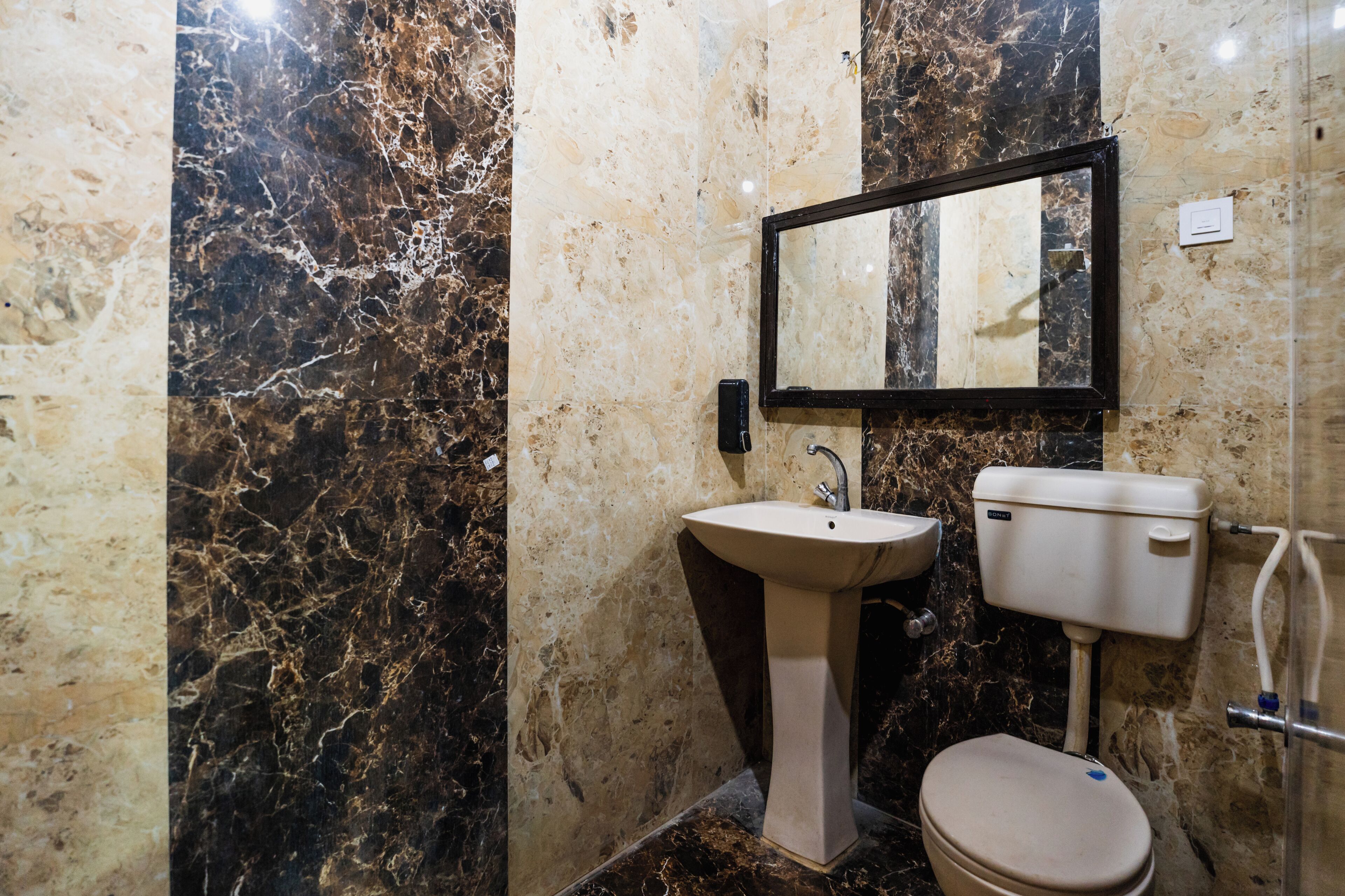 A bathroom with a marble wall, a sink, a toilet, and a mirror.