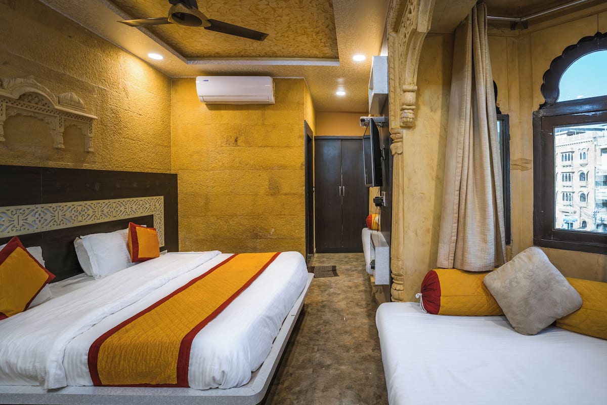 A hotel room with two beds, a ceiling fan, an air conditioning unit, and a view of the city through a window.