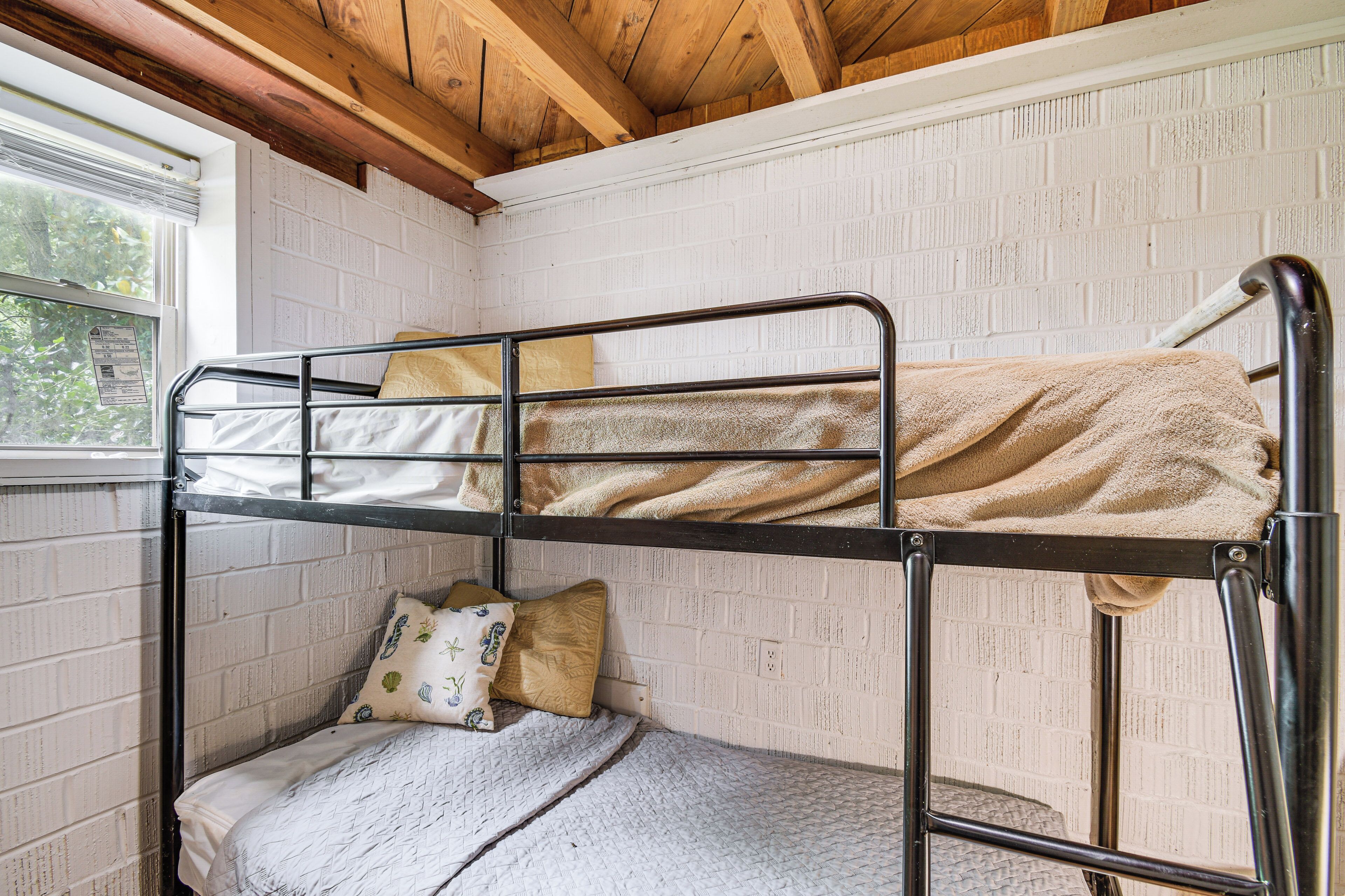 A bunk bed with a window, white brick walls, and wooden beams.