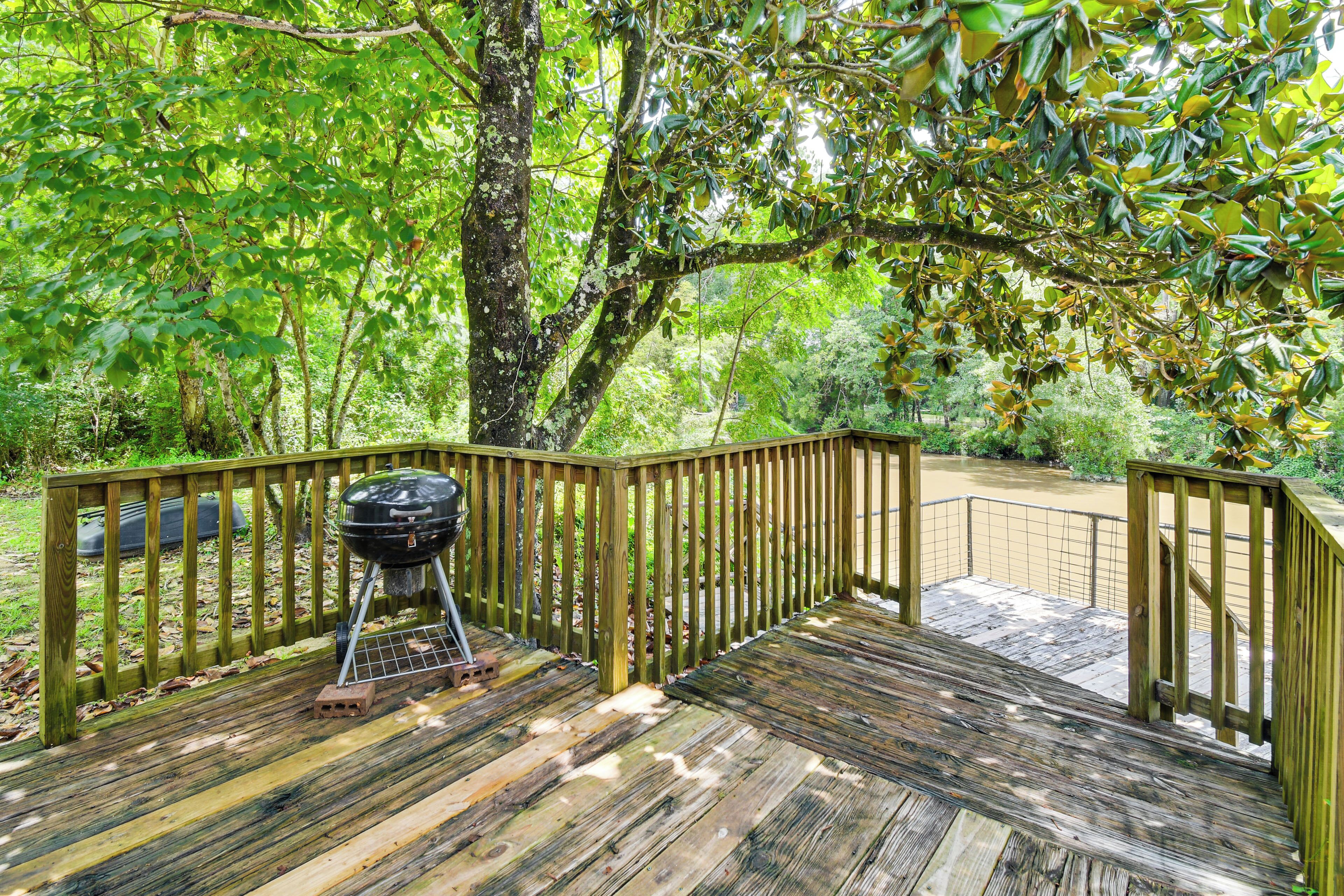 Une terrasse en bois avec un barbecue, entourée d’une végétation luxuriante.