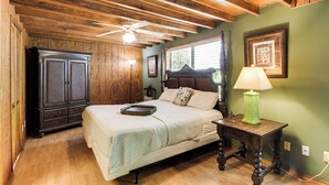 Quarto com teto de madeira, cama com bandeja, mesa de cabeceira com luminária e guarda-roupa.