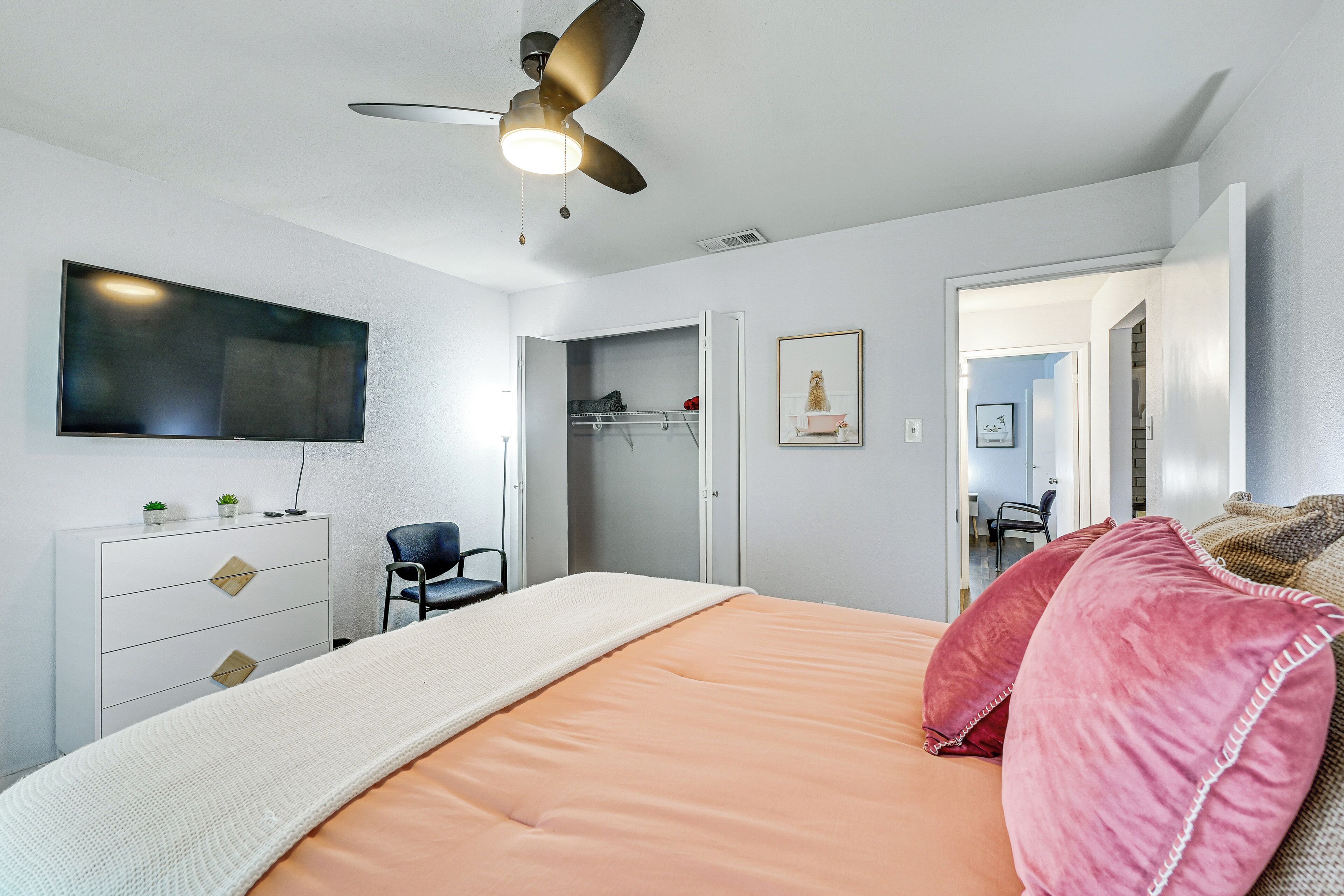 Een slaapkamer met een bed, een plafondventilator, een televisie, een kledingkast en een stoel.