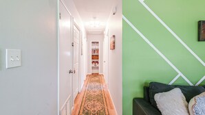 A hallway with a patterned carpet, a green wall with white lines, and a dark sofa with pillows. - Mid-century Gainesville Getaway: 3 Mi to UF Campus (Gainesville)